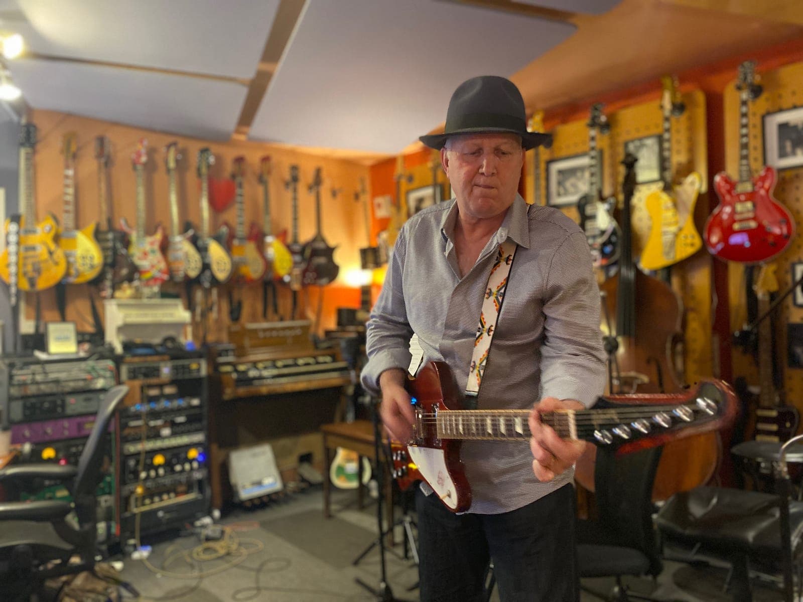 Michael Larkings playing a red electric guitar in a studio full of guitars